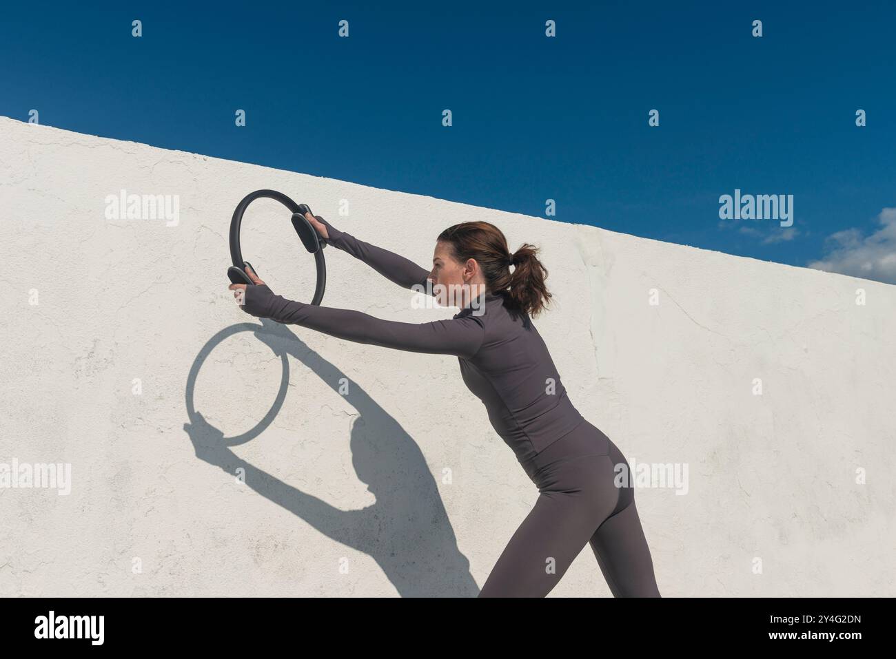 Sportliche Frau, die sich mit einem Pilates-Ring ausdehnt, Fitnesskonzept im Freien Stockfoto
