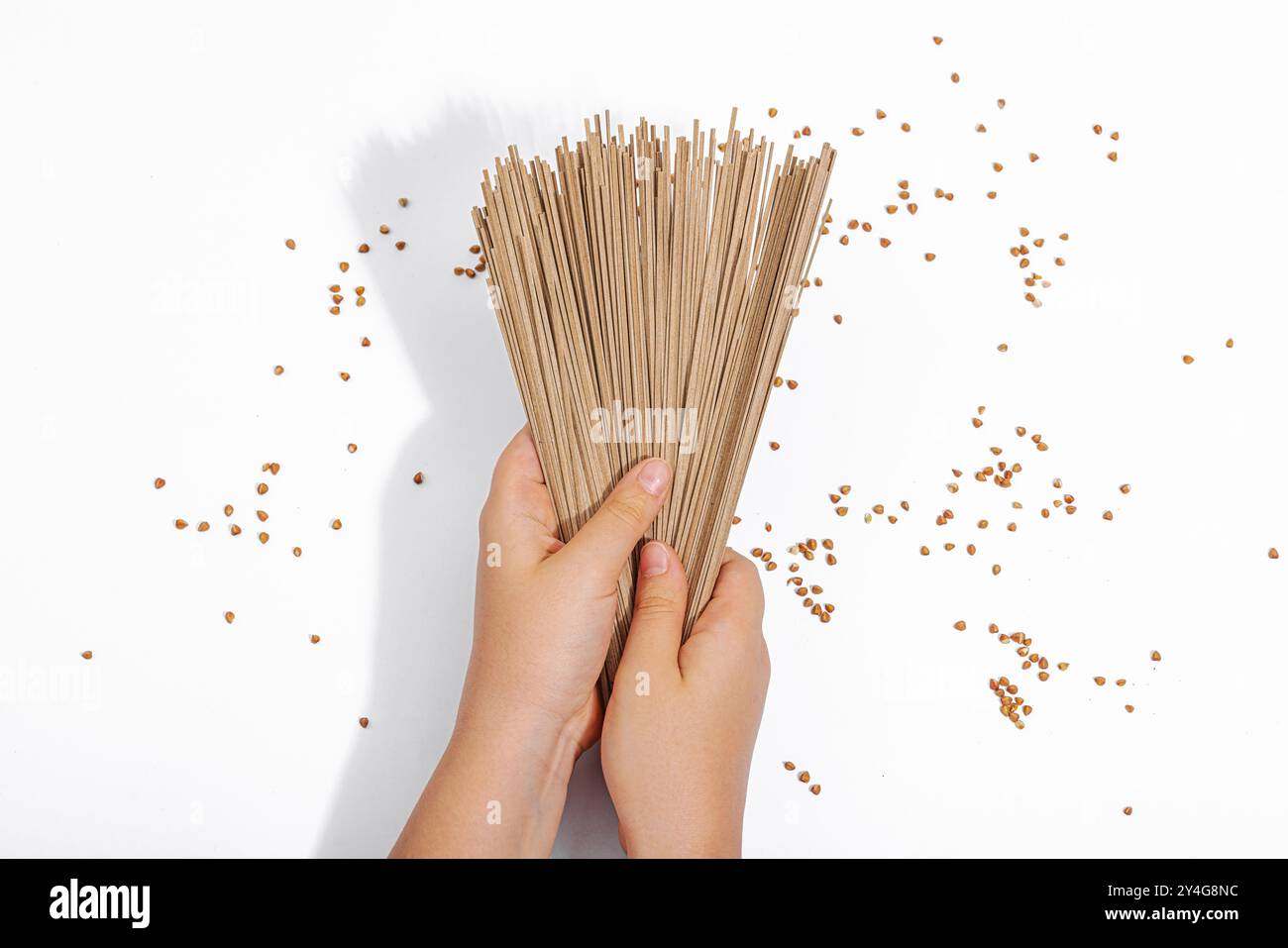 Kinderhände halten japanische Buchweizen-Soba-Nudeln. Klassische Zutat für die Zubereitung traditioneller Gerichte. Hartes Licht, dunkler Schatten, weißer Hintergrund, Stockfoto