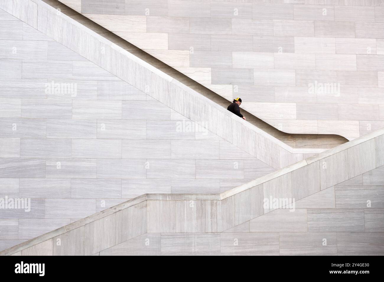National Gallery of Art Staircase Washington DC // WASHINGTON DC — Ein Besucher steigt die markante Treppe im Atrium des East Building in der National Gallery of Art hinab Das vom Architekten I.M. Pei entworfene modernistische Gebäude zeichnet sich durch markante geometrische Formen und ein Spiel von Licht und Schatten aus. Die Treppe, die in eine Steinmauer gebaut wurde, veranschaulicht Peis minimalistischen und dennoch dramatischen architektonischen Stil und schafft ein markantes visuelles Element im geräumigen Inneren des Museums. Stockfoto