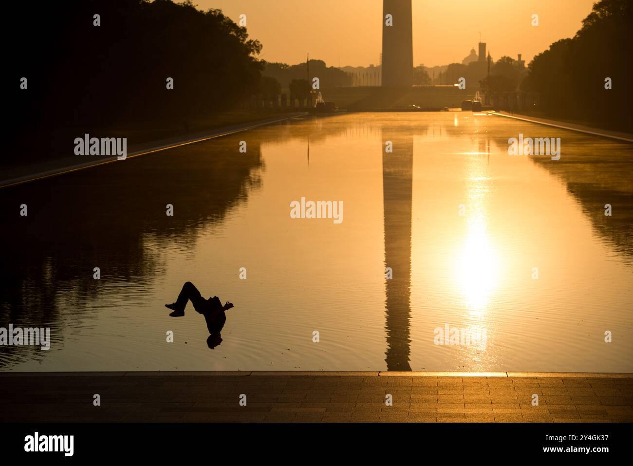 Washington D.C. // WASHINGTON D.C. – das Washington Monument, die Kuppel des US Capitol und der Reflecting Pool vom Lincoln Memorial aus gesehen bei Sonnenaufgang während der Frühlings- und Herbstnachtgleiche. Die Sonne geht perfekt auf die National Mall auf und strahlt ein warmes Leuchten über die berühmten Wahrzeichen. In dieser Aufnahme ist eine Person mit einer Silhouette versehen, die einen Backflip in der Nähe der Wasserlinie macht. Stockfoto