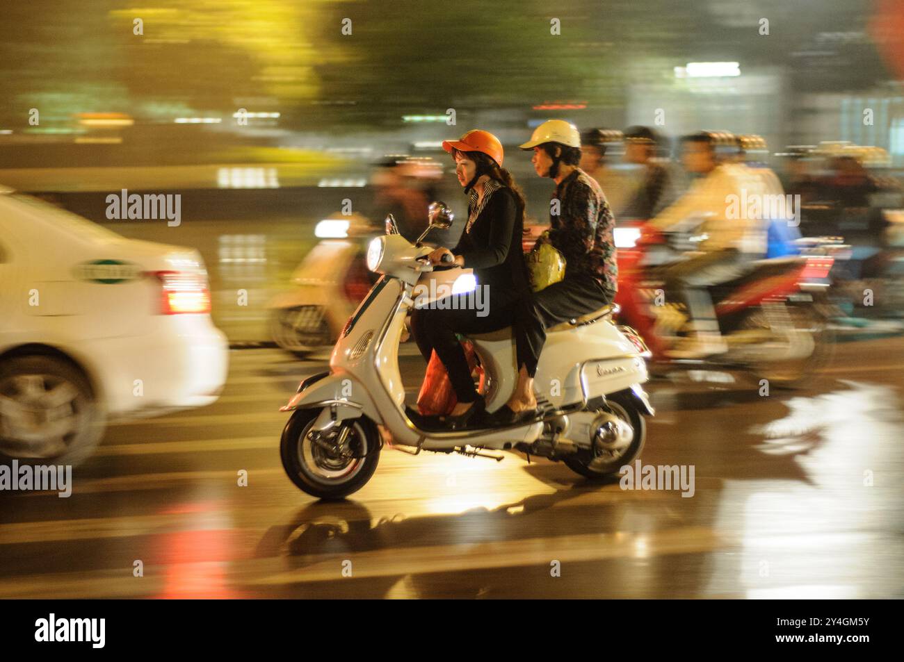 Motorroller auf der Straße Hanoi Vietnam // HANOI, Vietnam – Motorroller und Fahrräder drängen sich am Abend auf eine enge Straße in der Altstadt von Hanoi. Die belebte Szene zeigt das chaotische, aber lebendige Straßenleben, das typisch für Hanoi ist, während die Einheimischen die geschäftigen Straßen mit dem Motorrad oder dem Fahrrad erkunden. Stockfoto