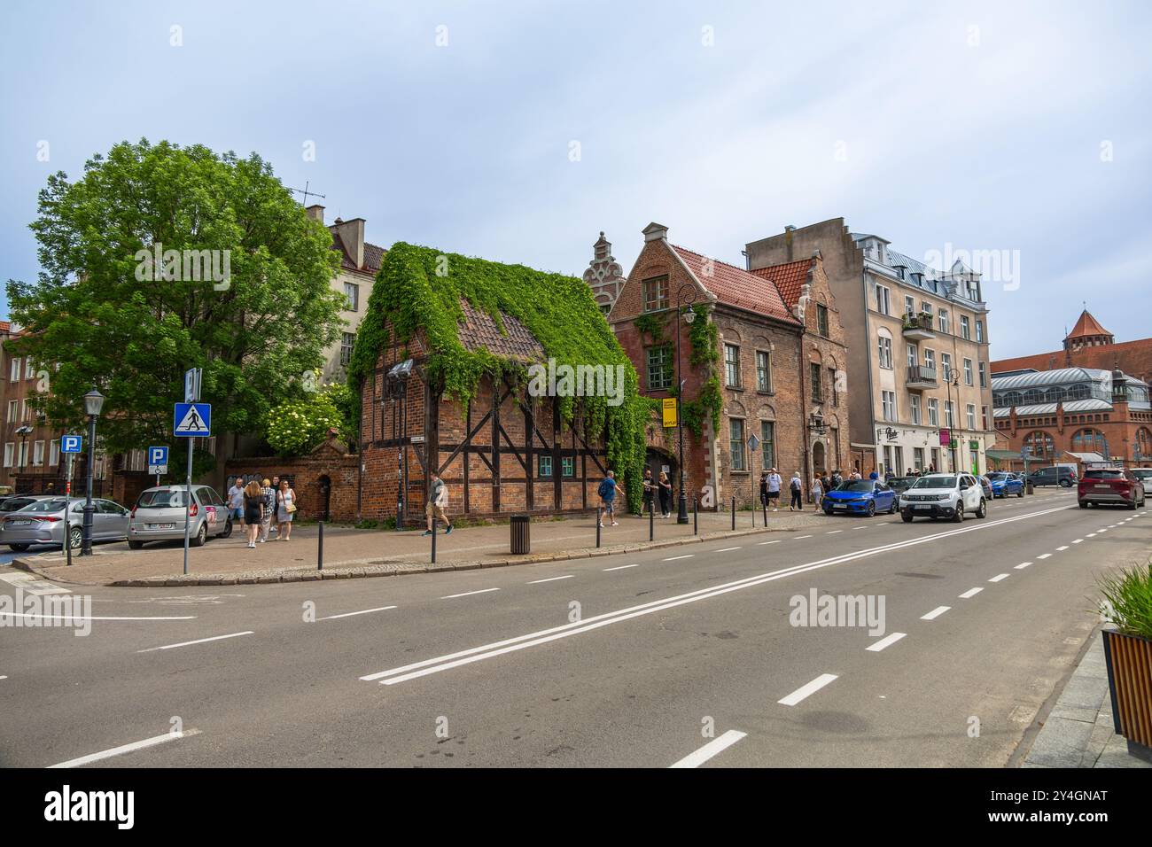 Blick auf die Straße in Danzig, Polen, mit einem historischen, mit Efeu bedeckten Haus mit traditioneller Backstein- und Holzarchitektur entlang einer befahrenen Straße. Stockfoto