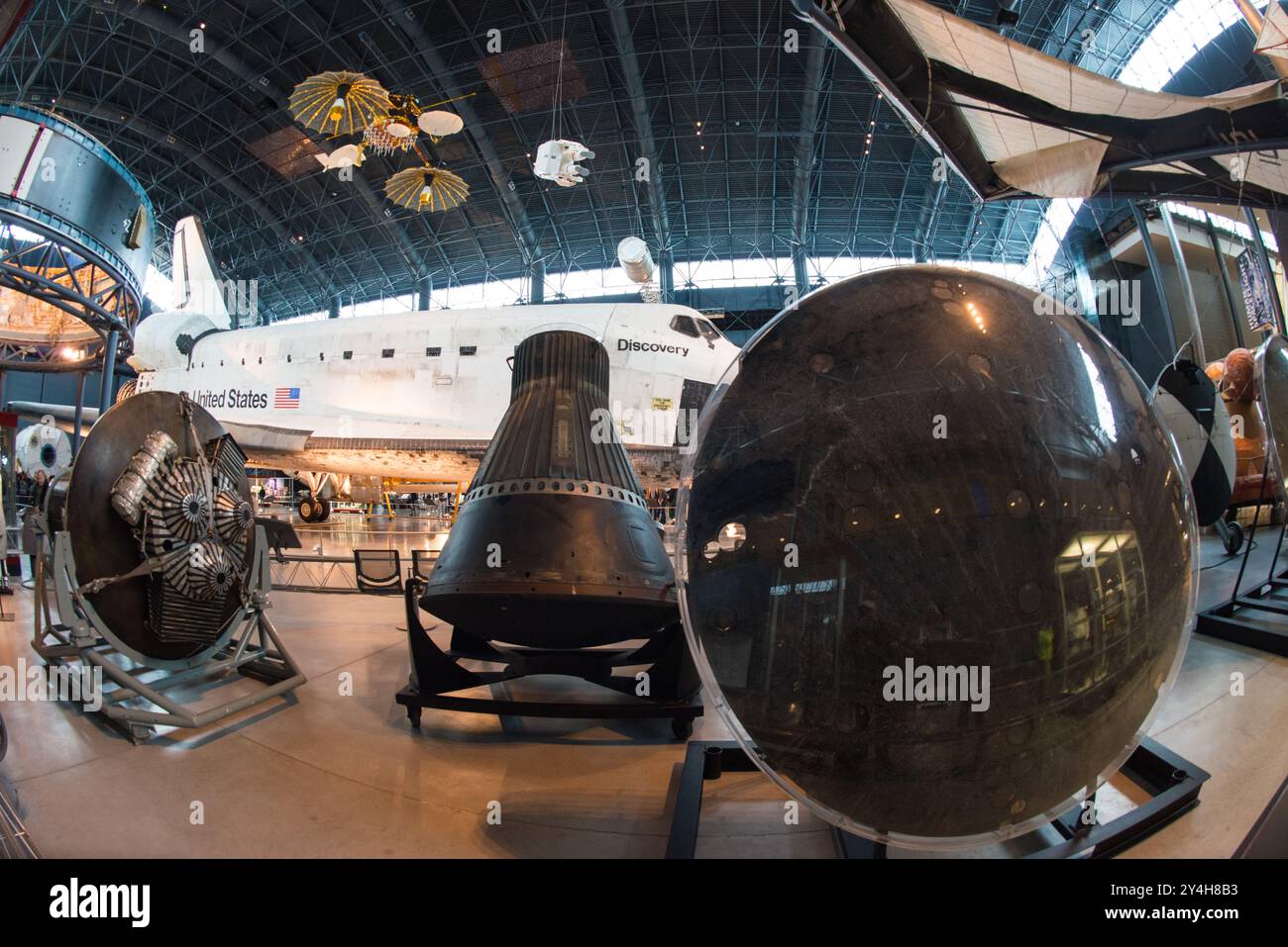 Space Shuttle Discovery Gemini Capsule Udvar-Hazy Center Chantilly Virginia | CHANTILLY, Virginia — Ein Fischaugenblick umrahmt den Hitzeschild einer Gemini-Kapsel im Vordergrund mit dem Space Shuttle Discovery dahinter im Steven F. Udvar-Hazy Center. Das Gemini-Programm, das zweite Projekt der NASA, flog zwischen 1965 und 1966 zehn bemannte Missionen und überbrückte die Lücke zwischen den Single-Astronaut-Flügen Mercury und dem Apollo-Mondprogramm. Stockfoto