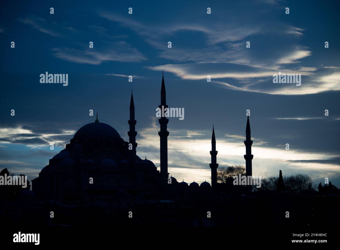 ISTANBUL, Türkei / Türkiye – Wispy Wolken fangen das silberne Licht der Abenddämmerung hinter der Silhouette der Süleymaniye Moschee ein. Die osmanische kaiserliche Moschee aus dem 16. Jahrhundert, entworfen vom Architekten Mimar Sinan, steht an prominenter Stelle auf Istanbuls drittem Hügel. Vier Minarette und die große zentrale Kuppel bilden das unverwechselbare Profil der Moschee vor dem Abendhimmel. Stockfoto