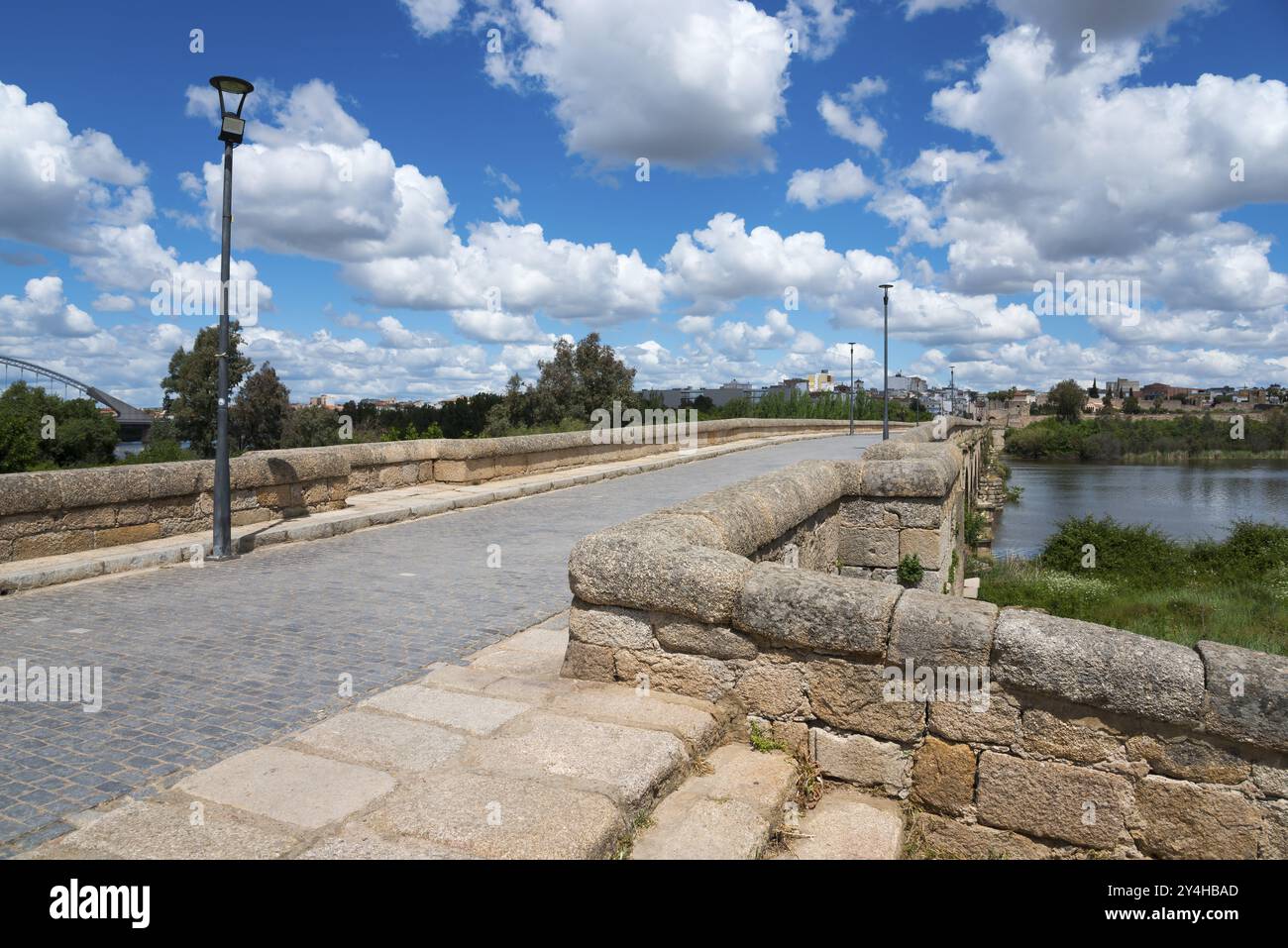 Blick auf eine alte Steinbrücke mit Kopfsteinpflaster vor einem klaren blauen Himmel und weißen Wolken, römische Brücke, Puente Romano, Bogenbrücke mit Keilstein vau Stockfoto