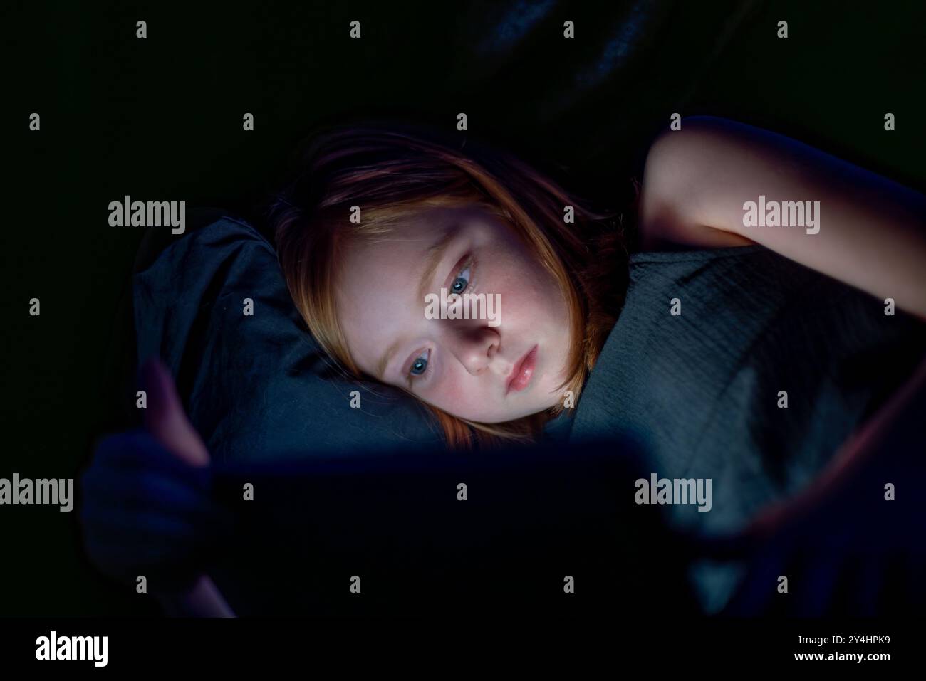 Porträt eines Mädchens bei schlechtem Licht, das nachts einen Bildschirm benutzt, mit blauem Licht, das auf ihrem Gesicht reflektiert. Stockfoto