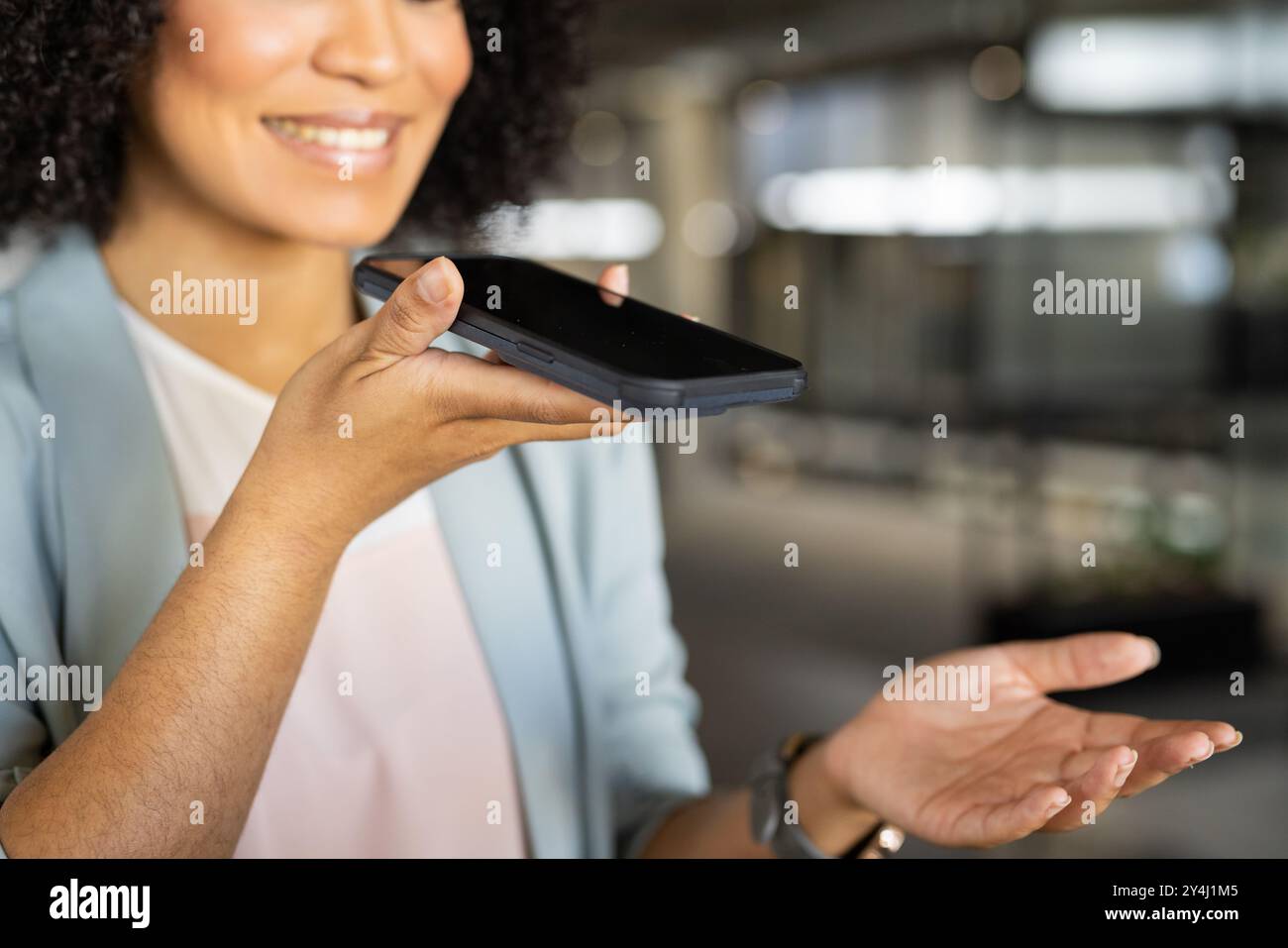 Smartphone in der Hand, Geschäftsfrau lächelnd und mit Sprachassistent im Büro Stockfoto