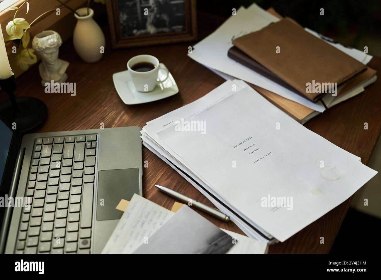 Übersichtliche Einrichtung im Home Office mit Laptop, Kaffeetasse und Papierstapel, die ordentlich auf dem Schreibtisch platziert sind. Gemütlicher, von einer Lampe beleuchteter Arbeitsbereich für produktive Arbeit Stockfoto