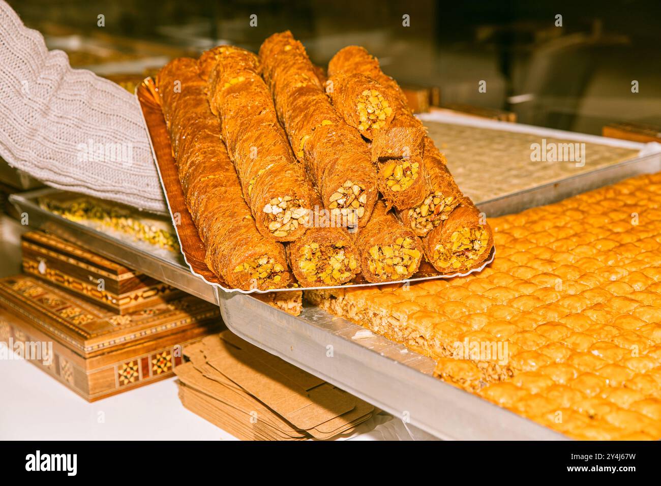 Mit traditionellem Gebäck aus dem Nahen Osten, knusprigen süßen Brötchen, serviert mit Nüssen, goldenen Texturen, auf Tablett, Baklava, reichhaltige Desserts, Bäckerei-Schaufenster Stockfoto
