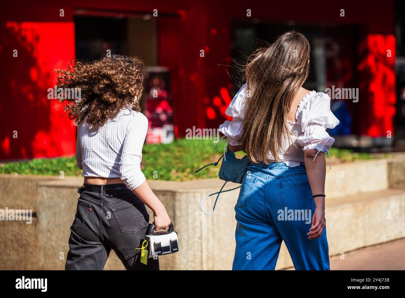 Zwei weiße brasilianische Mädchen, in weißen Blusen und Jeanshosen gekleidet, laufen zügig in Savassi, Belo Horizonte, Brasilien. Stockfoto