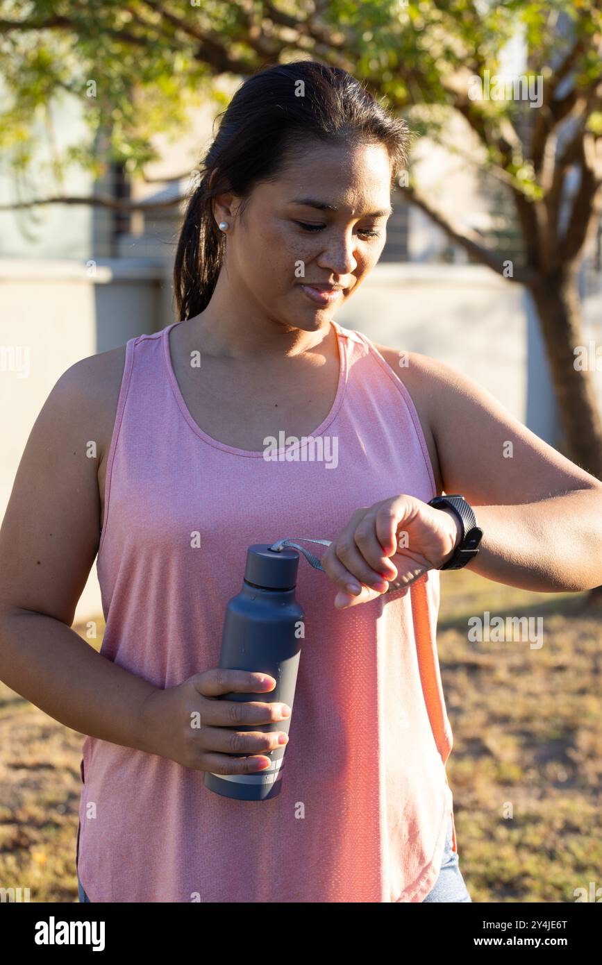 Smartwatch überprüfen und Wasserflasche halten, Frau genießt Outdoor-Training Stockfoto