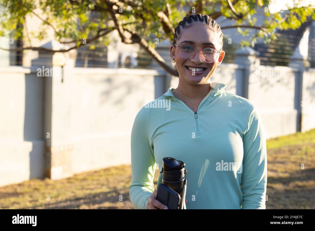Lächelnde Frau, die Wasserflasche und Smartphone hält und Outdoor-Übungen genießt Stockfoto