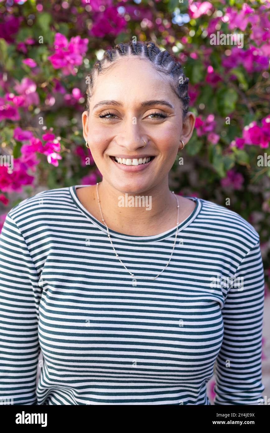 Lächelnde Frau in gestreiftem Hemd, die draußen vor blühenden Blumen steht Stockfoto