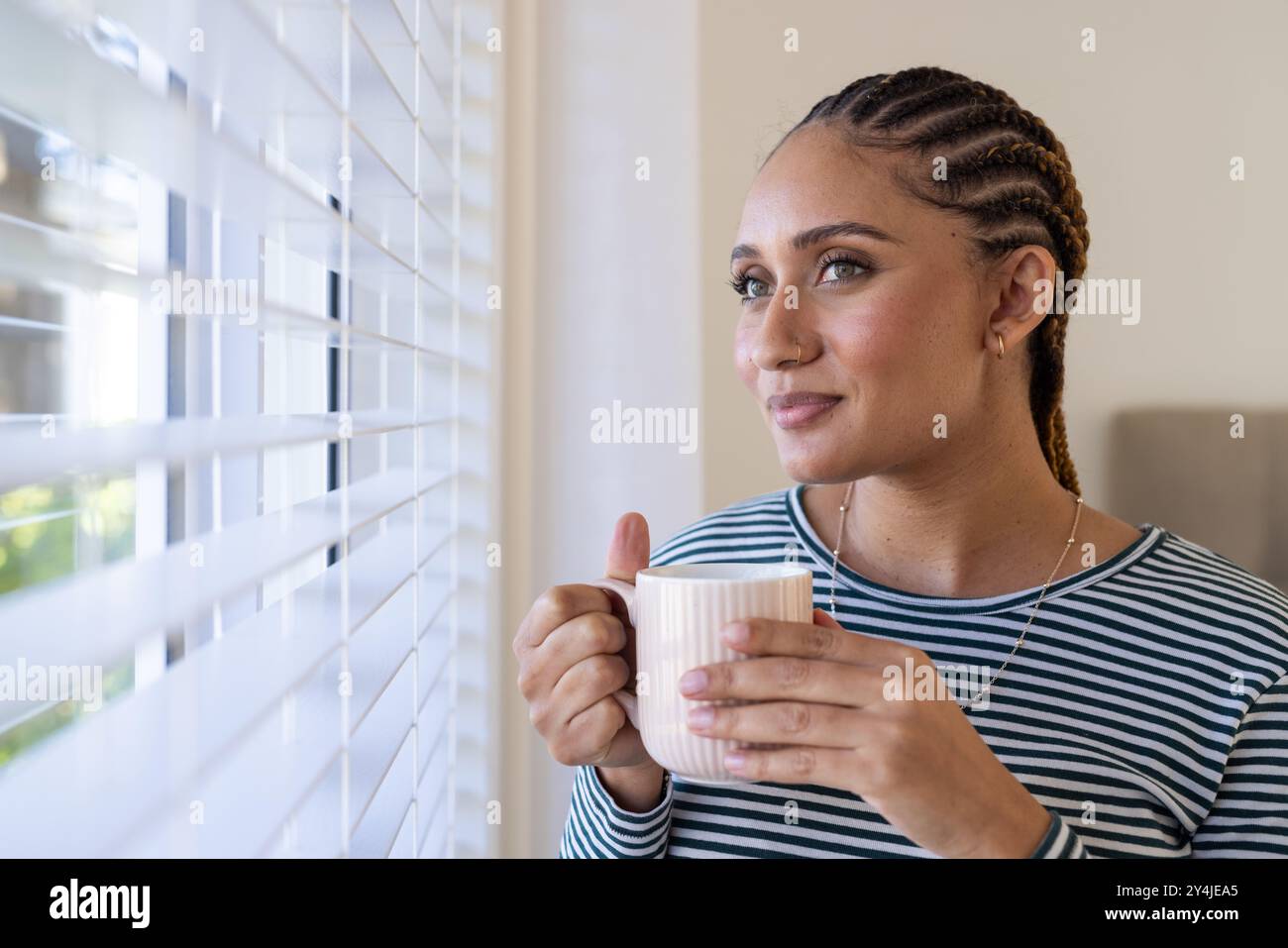 Die Kaffeetasse hält, die Frau blickt aus dem Fenster und genießt den Morgen Stockfoto