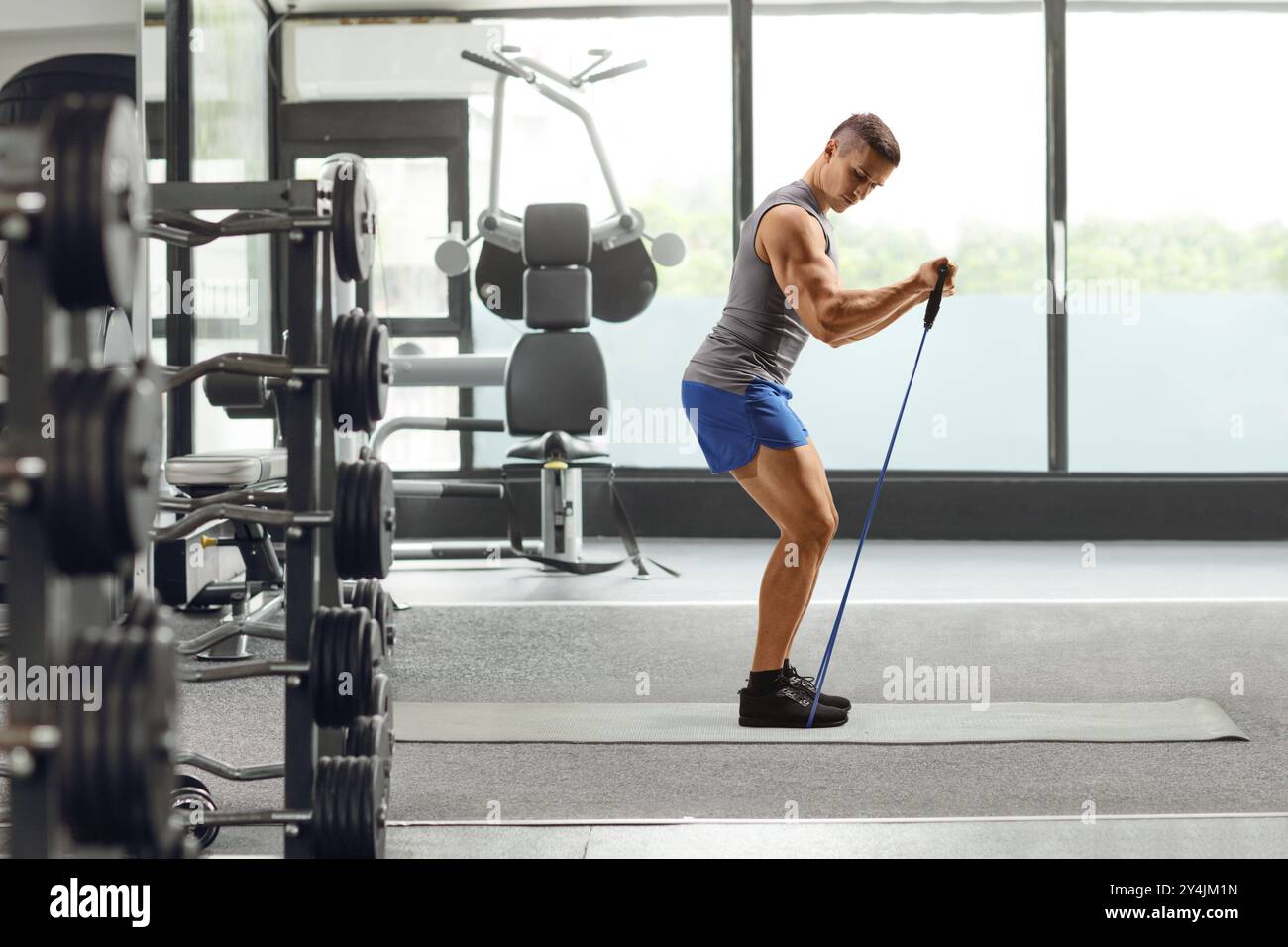 Profilaufnahme eines Mannes, der mit einem Widerstandsband auf einer Matte in einem Fitnessstudio trainiert Stockfoto