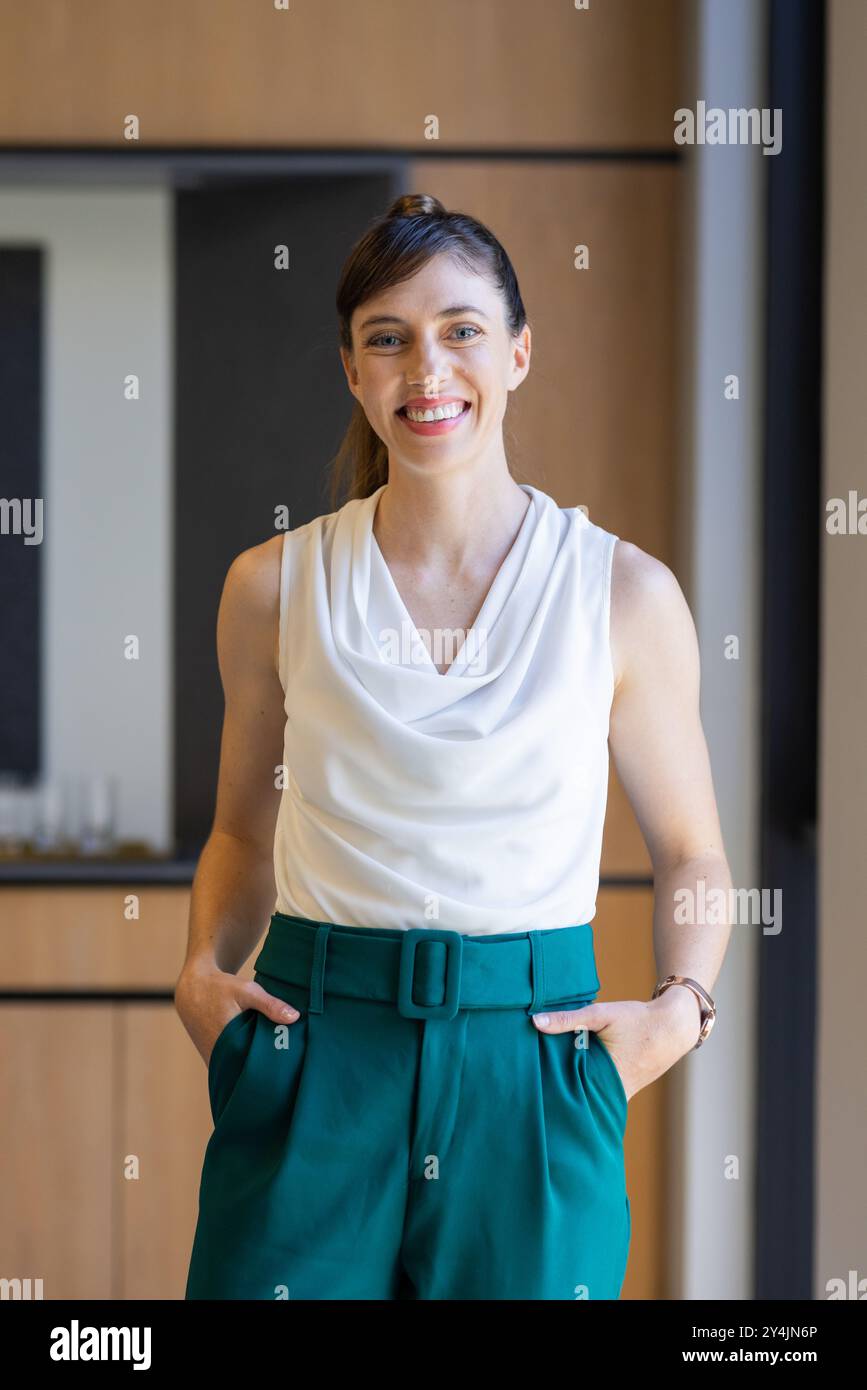 Lächelnd im Büro, Geschäftsfrau in weißer Bluse und grüner Hose, Hände in Taschen Stockfoto