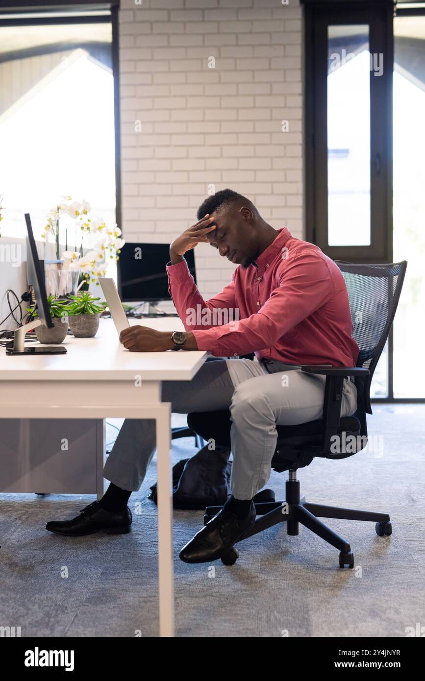 Stressiger Geschäftsmann, der am Schreibtisch sitzt und sich in einem modernen Büro ein Tablet anschaut Stockfoto