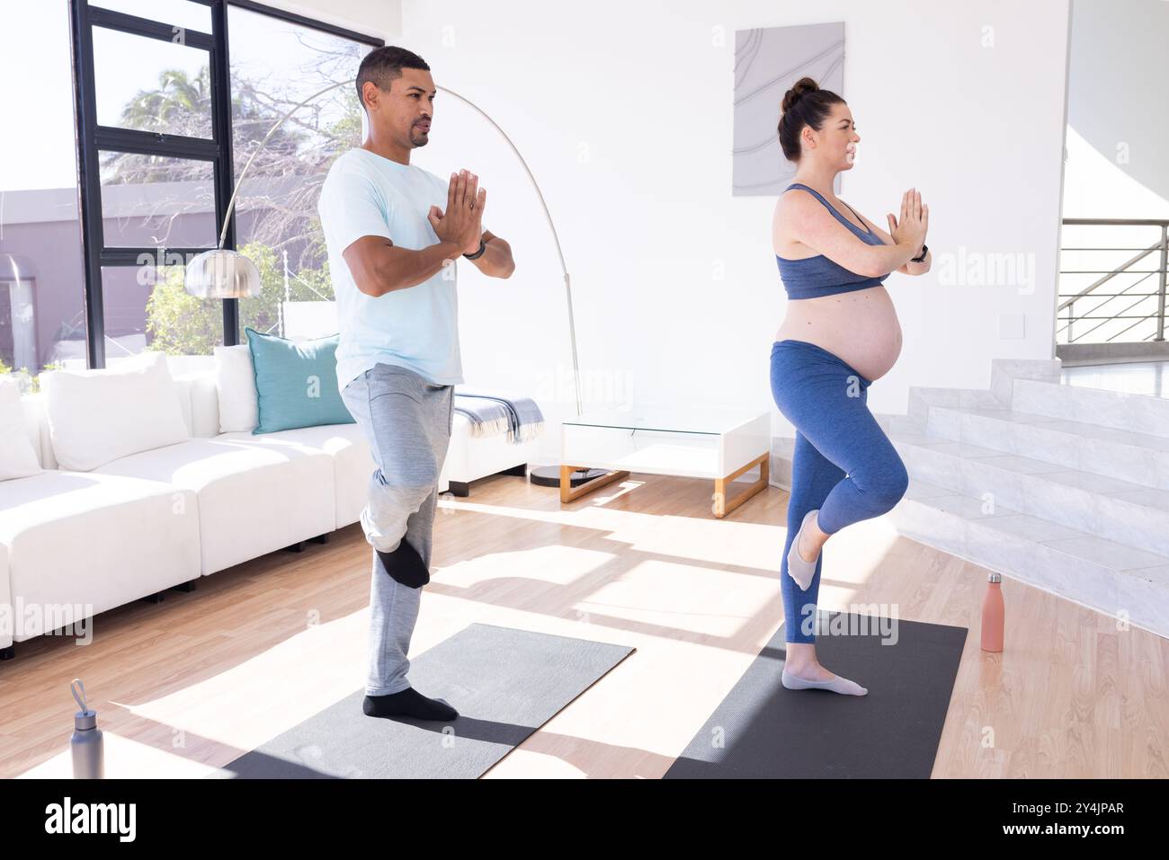 Zu Hause, multirassisches Paar, praktizierendes Yoga, schwangere Frau und Mann balancieren in Baumhaltung Stockfoto