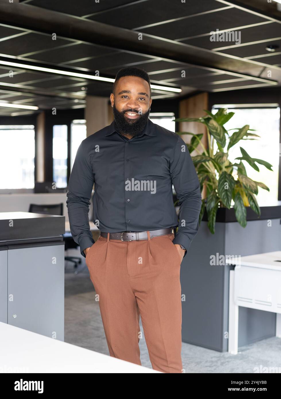 Lächelnder afroamerikanischer Geschäftsmann im modernen Büro, mit Händen in Taschen Stockfoto