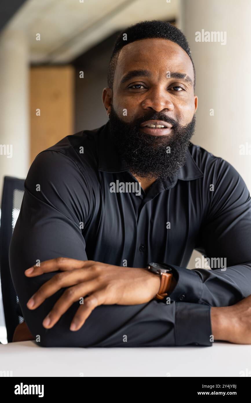Lächelnder afroamerikanischer Geschäftsmann in schwarzem Hemd am Schreibtisch im modernen Büro Stockfoto