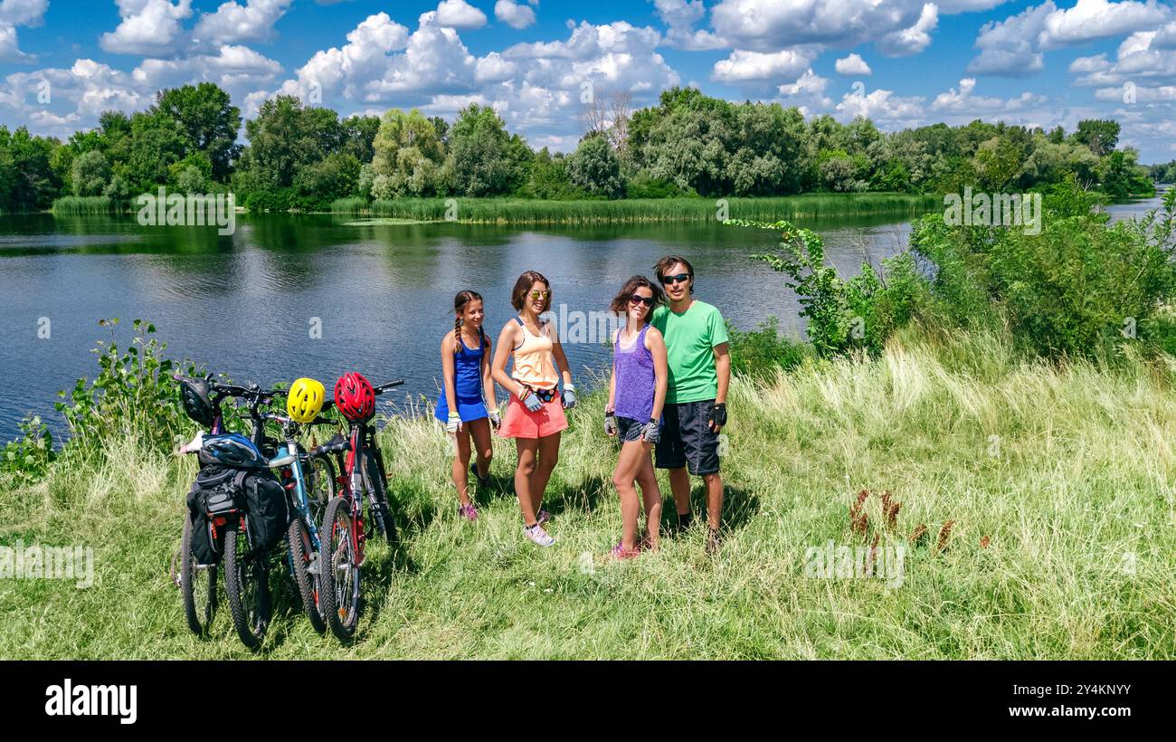 Familie auf Fahrrädern im Freien, aktive Eltern und Kinder auf Fahrrädern, aus der Vogelperspektive auf glückliche Familie mit Kindern, die sich in der Nähe des wunderschönen Flusses entspannen Stockfoto