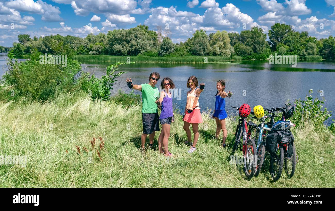 Familie auf Fahrrädern im Freien, aktive Eltern und Kinder auf Fahrrädern, aus der Vogelperspektive auf glückliche Familie mit Kindern, die sich in der Nähe des wunderschönen Flusses entspannen Stockfoto
