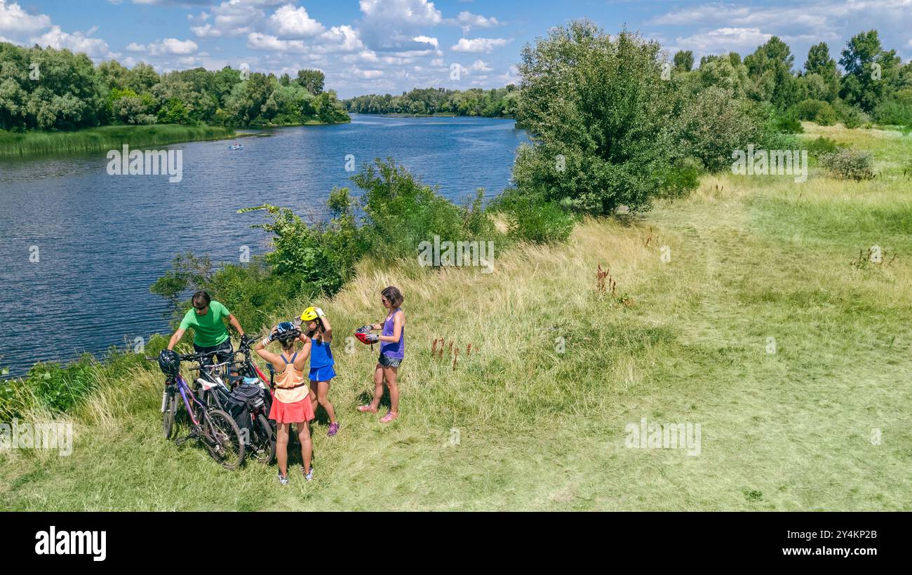 Familie auf Fahrrädern im Freien, aktive Eltern und Kinder auf Fahrrädern, aus der Vogelperspektive auf glückliche Familie mit Kindern, die sich in der Nähe des wunderschönen Flusses entspannen Stockfoto