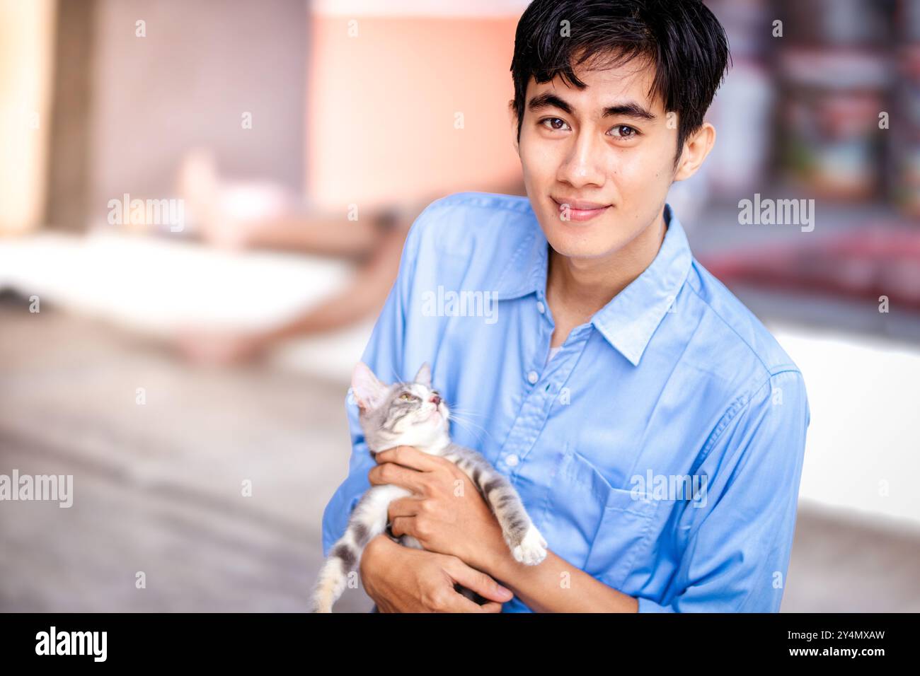 Ein Kerl lächelt, während er seine Katze umarmt. Schöne Männer und ein süßes Kätzchen. Stockfoto