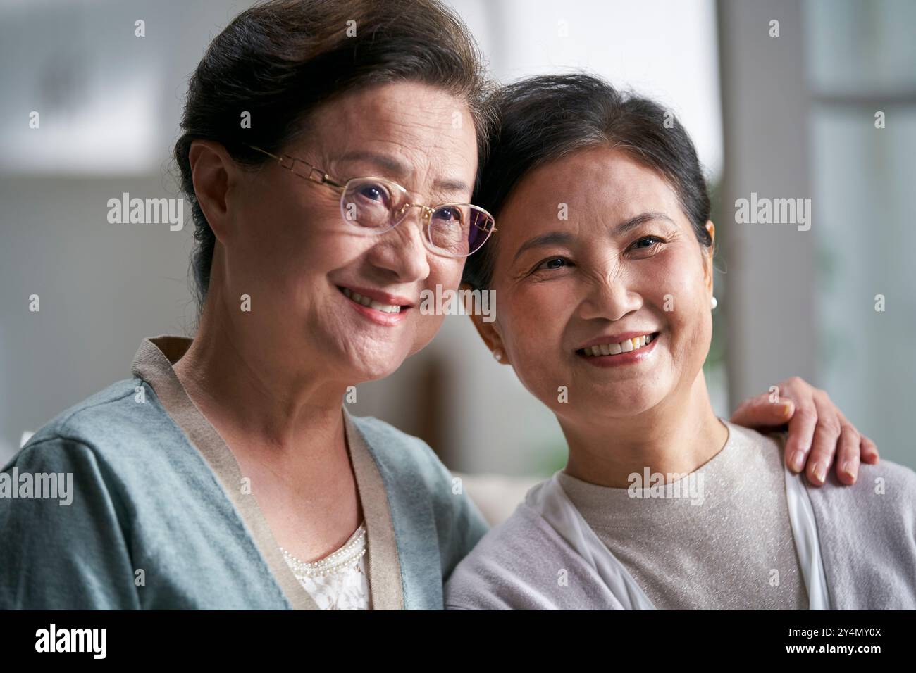 Porträt von zwei älteren asiatischen Frauen, die zu Hause glücklich und lächelnd auf der Couch sitzen Stockfoto