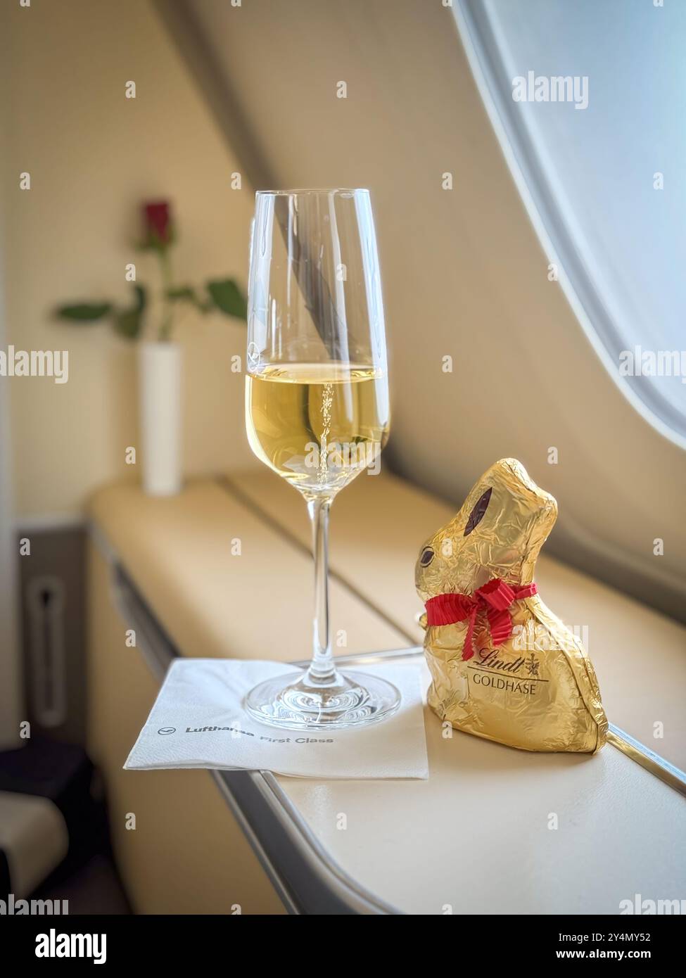 München, Deutschland - 29. März 2024: Lufthansa First Class Glas Champagner mit Schokoladen-osterhase Stockfoto