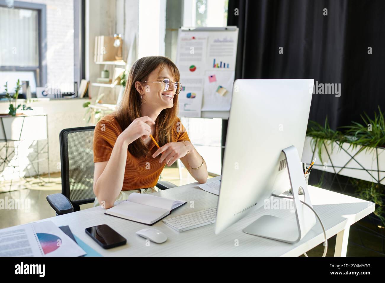 Eine nicht binäre Person lächelt beim Brainstorming an ihrem eleganten Schreibtisch. Stockfoto