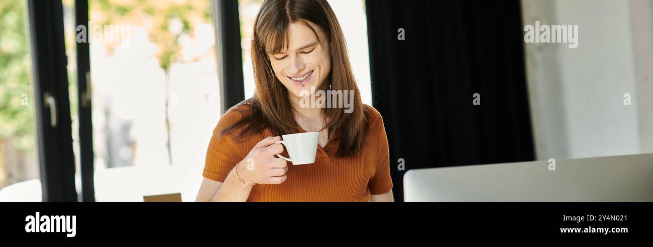 Eine nicht binäre Person lächelt mit Kaffee in einem hellen, stilvollen Arbeitsbereich. Stockfoto