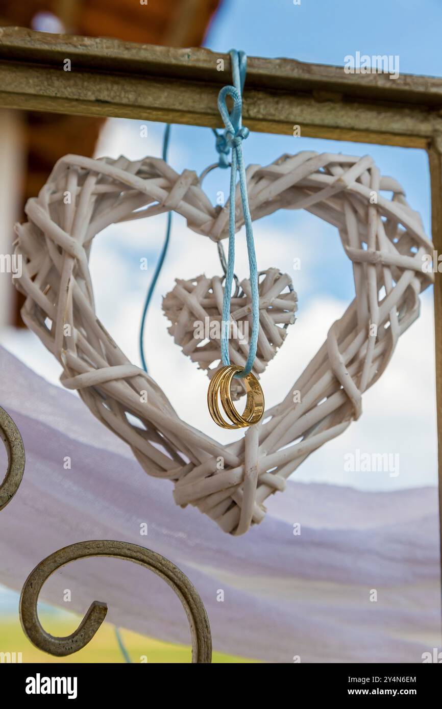 Nahaufnahme von zwei Eheringen, die vor einem Herzen hängen. Weichzeichner Stockfoto