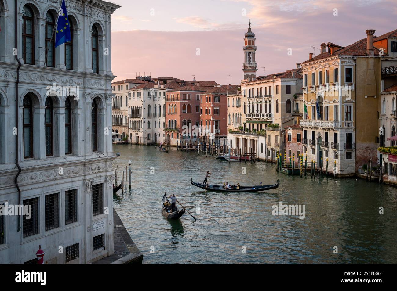 Blick von der Rialto-Brücke auf Gondoliere, die bei Sonnenuntergang auf Booten im Canale Grande von Venedig in Italien rudern Stockfoto