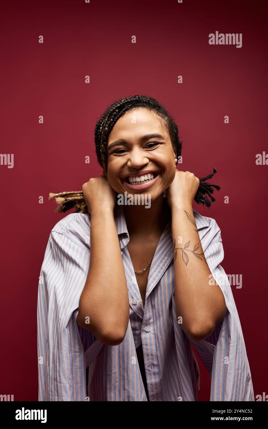 Eine junge afroamerikanische Frau mit geflochtenen Haaren lächelt hell und hält ihr Haar in einem Studio-Setting spielerisch. Stockfoto