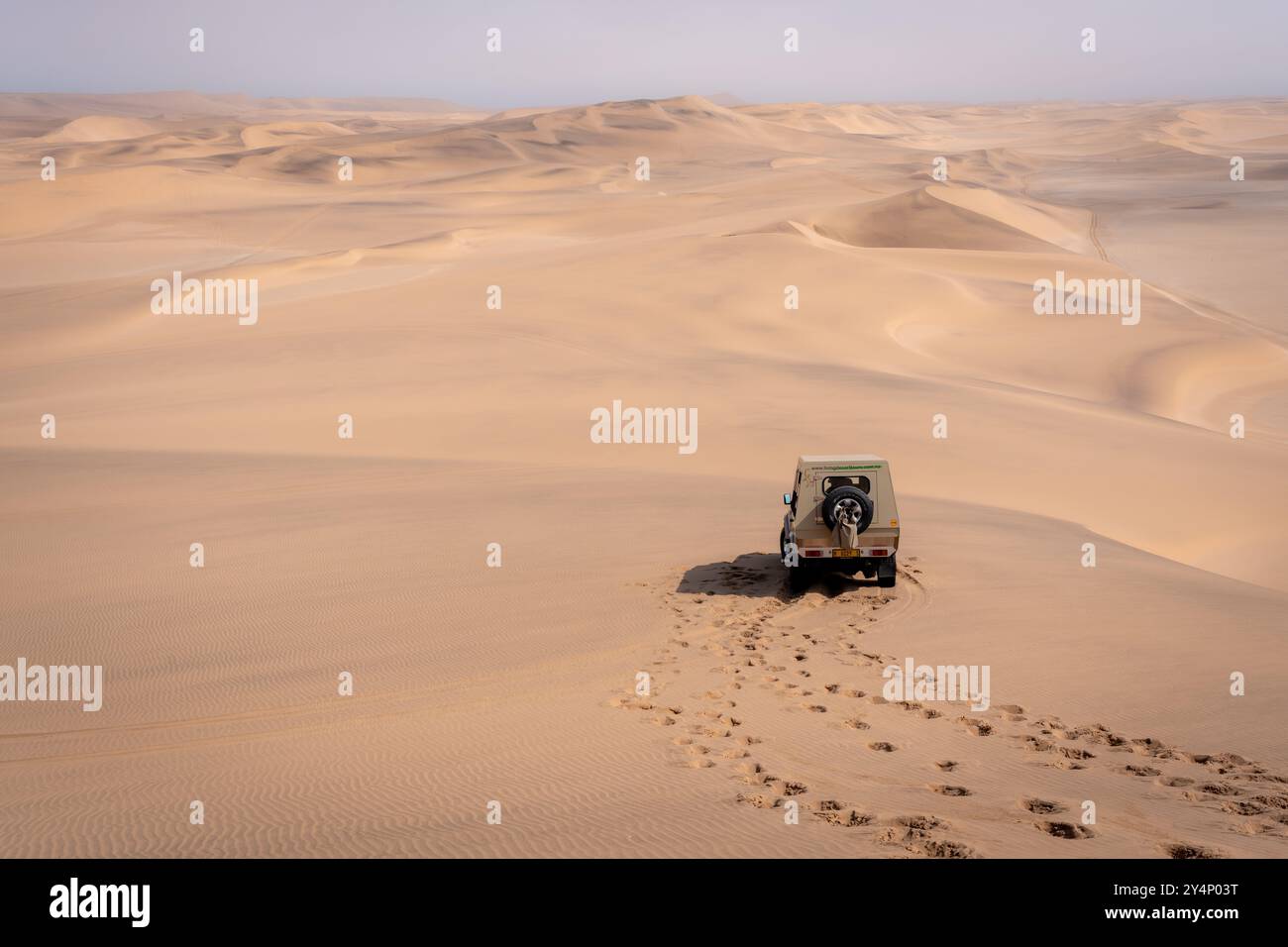 Ein Safari-Jeep parkte auf halbem Weg auf einer Sanddüne mit Fußspuren, die zu dem Ort führen, an dem der Fotograf in der Wüste in der Nähe von Swakopmund, Namibia, stand Stockfoto