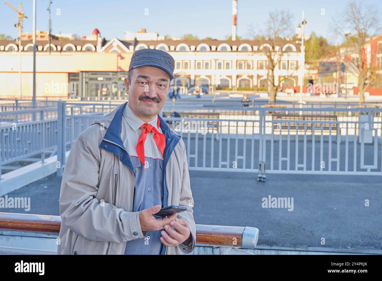 Straßenporträt eines hochrangigen asiatischen lächelnden glücklichen Mannes in roter Pionierkrawatte, ehemaliges Mitglied der Pionierorganisation der Kinder in der Sowjetunion. Blick auf die Kurvenscheibe Stockfoto