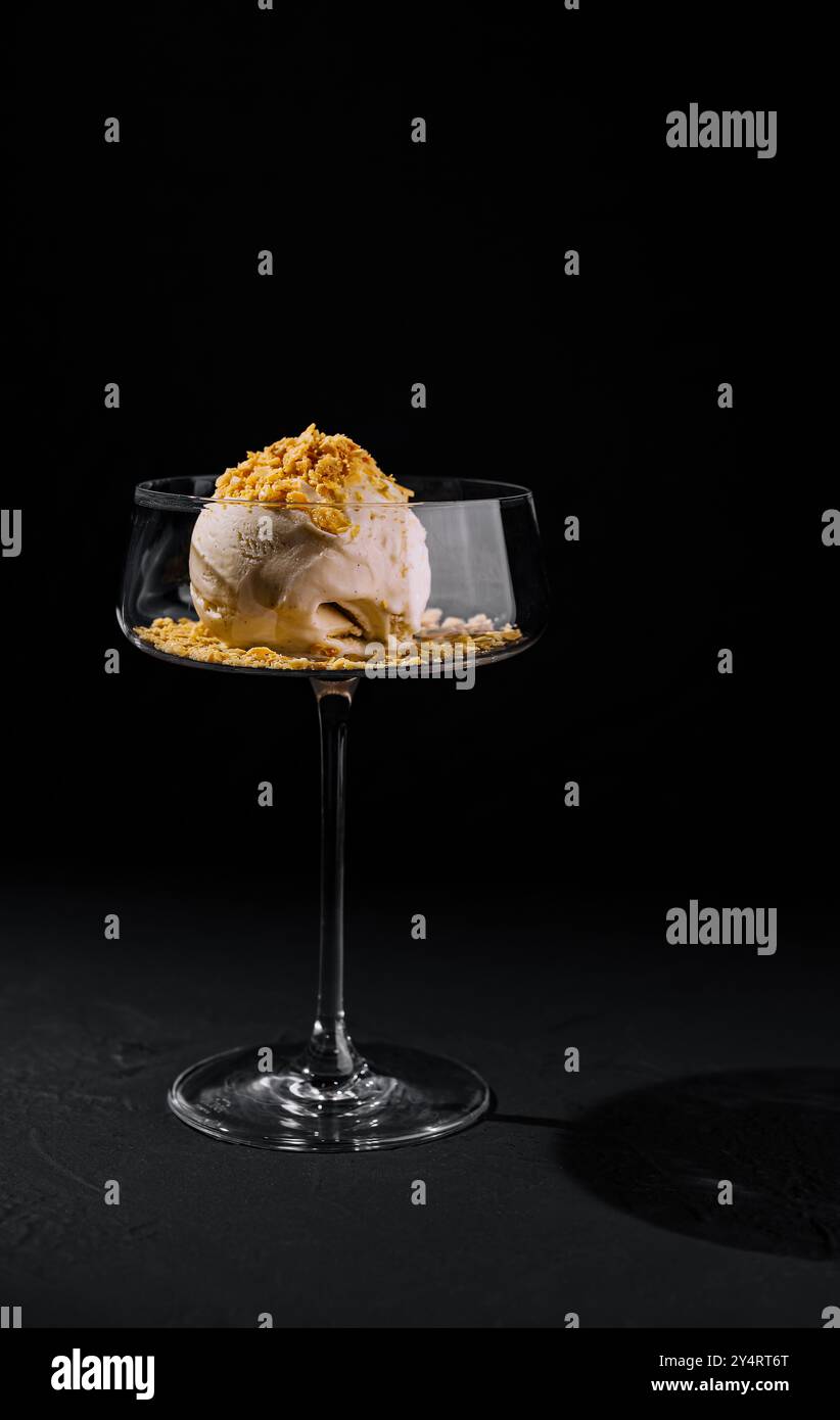 Kunstvoll überzogenes Eisdessert mit Crumble-Belag in einem stilvollen Coupé-Glas auf dunklem Hintergrund Stockfoto