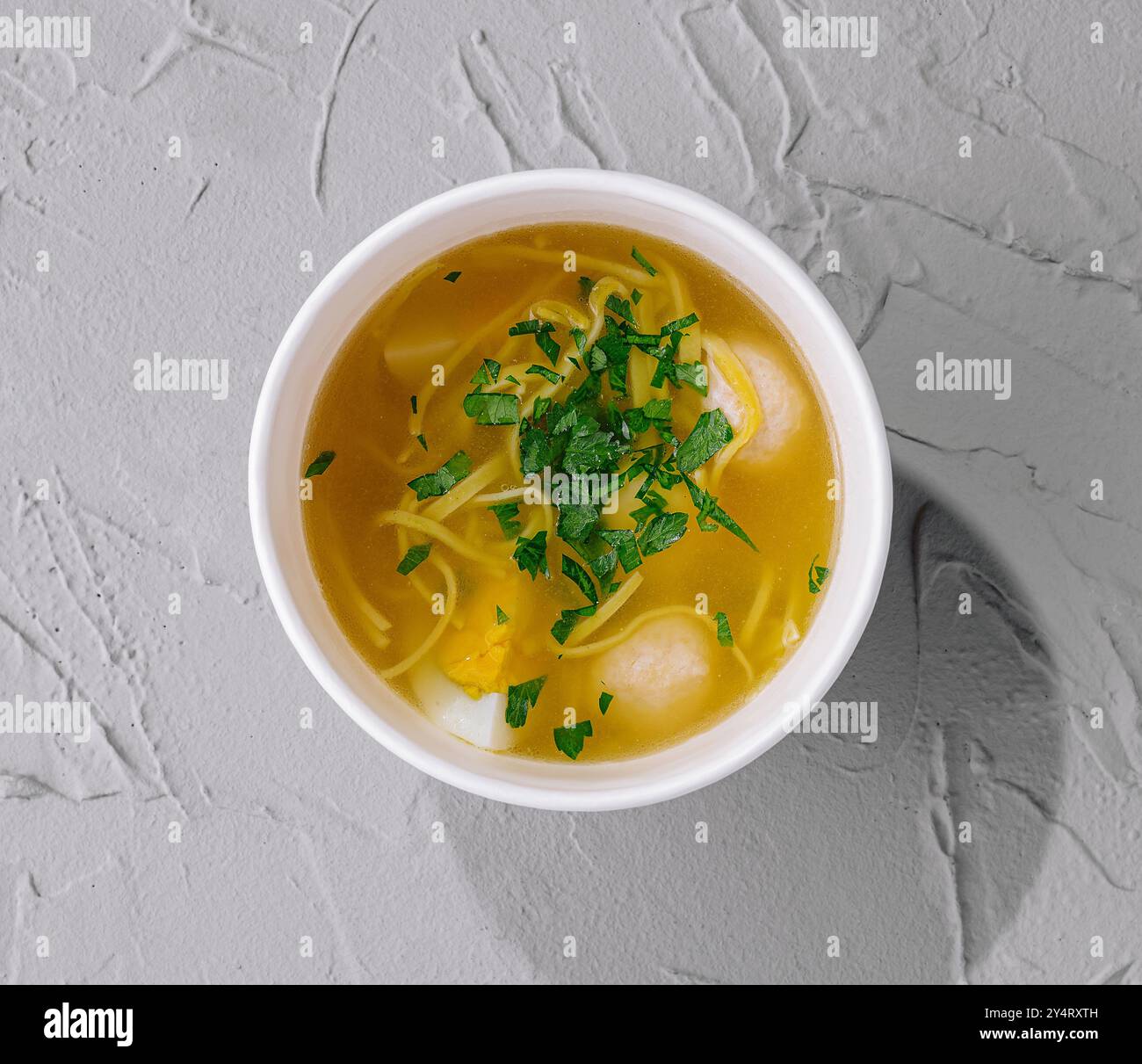 Blick von oben auf eine gemütliche Schüssel mit Hühnernudelsuppe, garniert mit Petersilie auf einer strukturierten Oberfläche Stockfoto