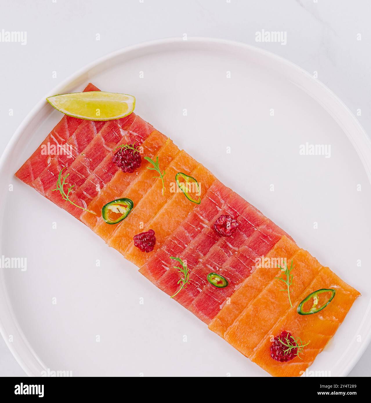 Blick von oben auf einen Teller Lachscarpaccio, garniert mit Limette und jalapeсo-Scheiben auf einem weißen Tisch Stockfoto