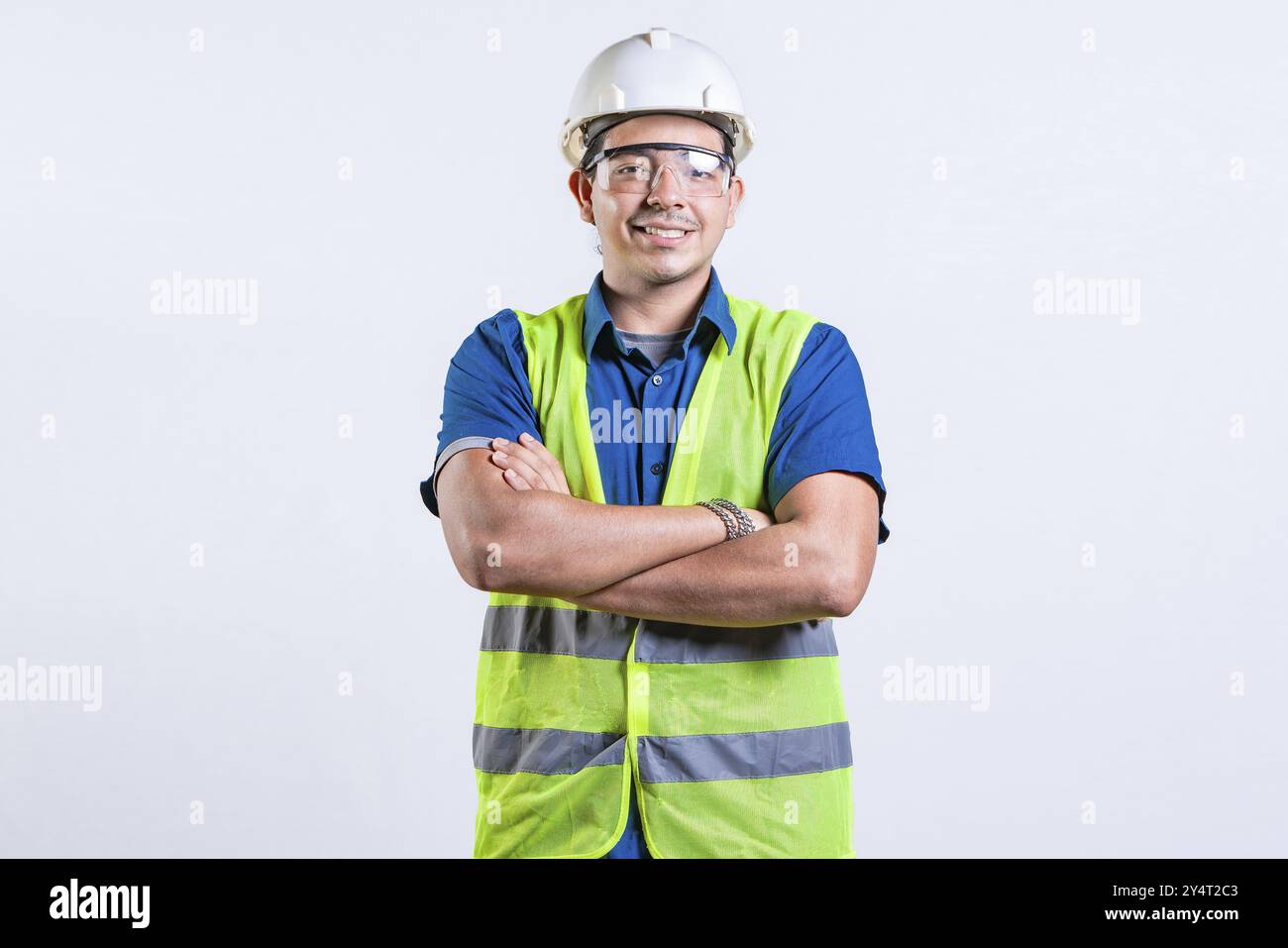 Porträt eines lächelnden lateinischen Ingenieurs mit gekreuzten Armen. Junger latein-Ingenieur mit Helm und Weste isoliert Stockfoto