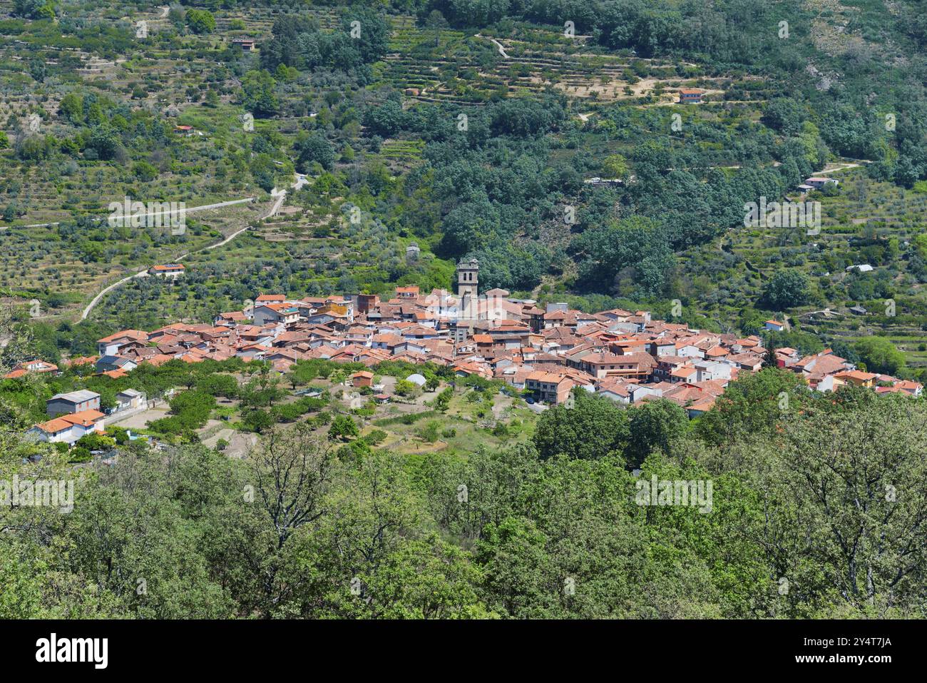 Ein kleines Dorf mit roten Dächern in einem grünen Tal, umgeben von Bergen und dichter Vegetation unter blauem Himmel, Garganta la Olla, Caceres, Caceres, Stockfoto