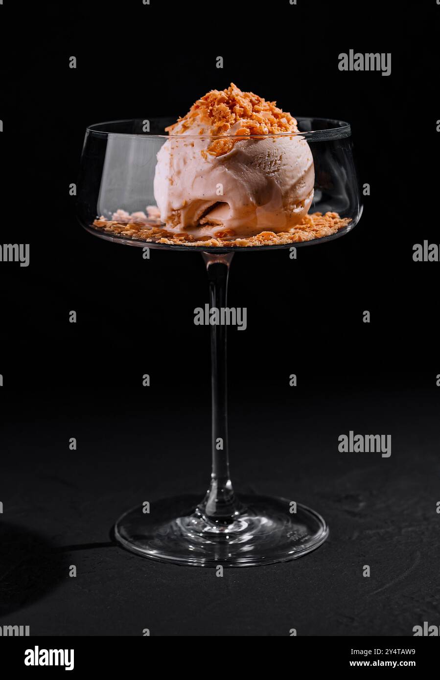 Kunstvoll überzogenes Eisdessert mit Crumble-Belag in einem stilvollen Coupé-Glas auf dunklem Hintergrund Stockfoto