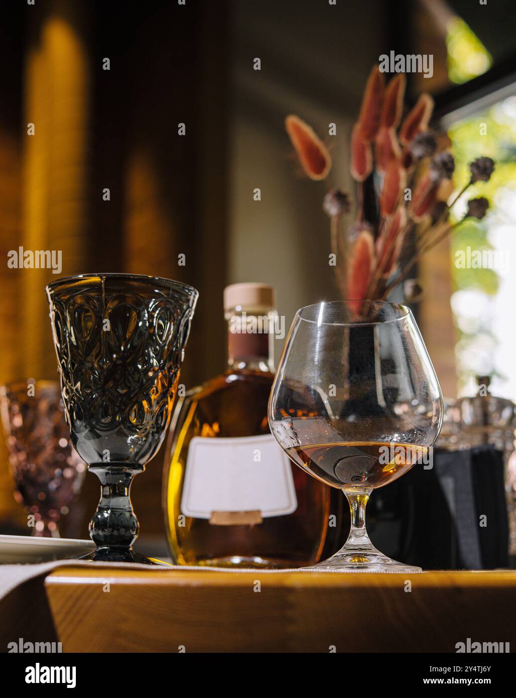 Luxuriöse Spirituosenflasche mit stilvollen Gläsern auf einem Holztisch vor warmer Kulisse Stockfoto