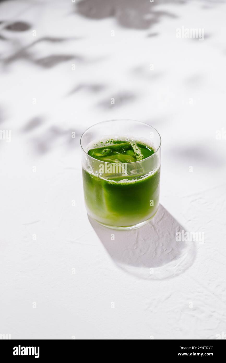 Erfrischende Eismatcha Latte sitzt auf einem weißen Tisch mit Schatten von Blättern im Hintergrund Stockfoto