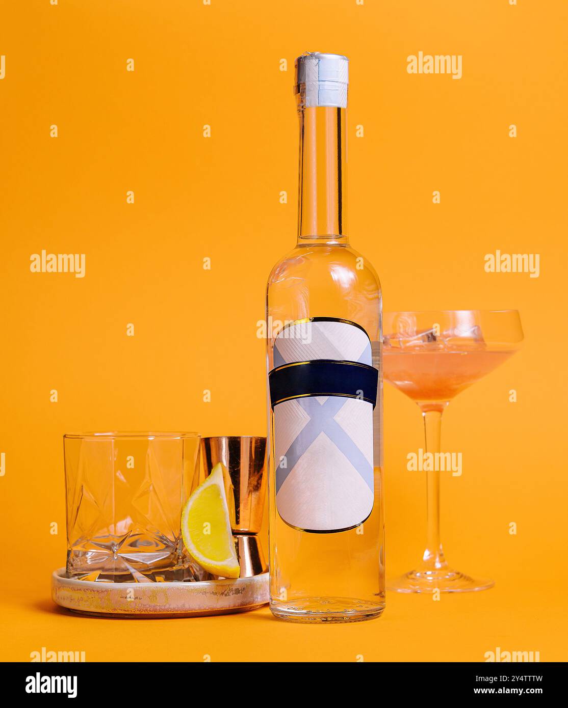 Flasche klarer Schnaps auf orangefarbenem Hintergrund mit Cocktailglas und Jigger Stockfoto