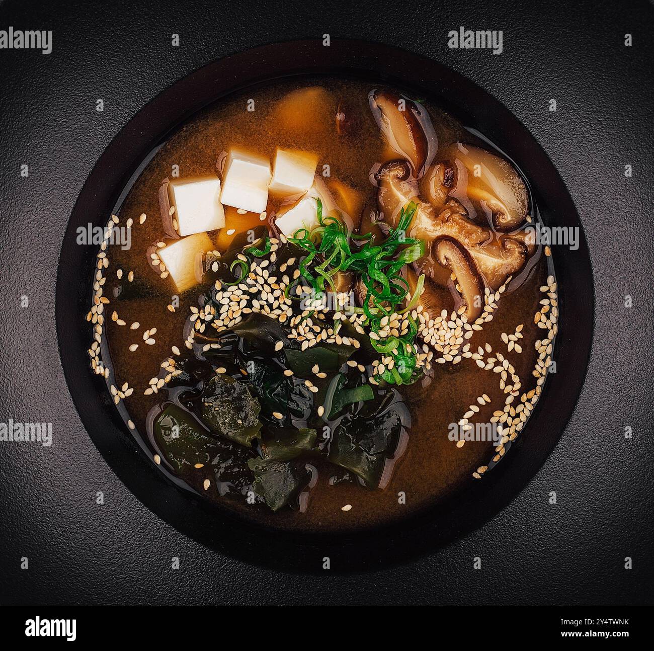 Eine köstliche Schüssel Miso-Suppe wird in einer schwarzen Schüssel mit Tofu, Pilzen, Algen und Sesamsamen serviert Stockfoto