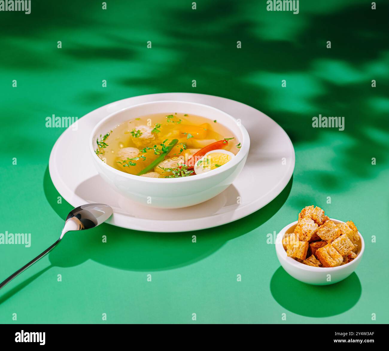 Dampfende Hühnersuppe mit Fleischbällchen, Gemüse und Kräutern, serviert mit Croutons auf grünem Hintergrund Stockfoto