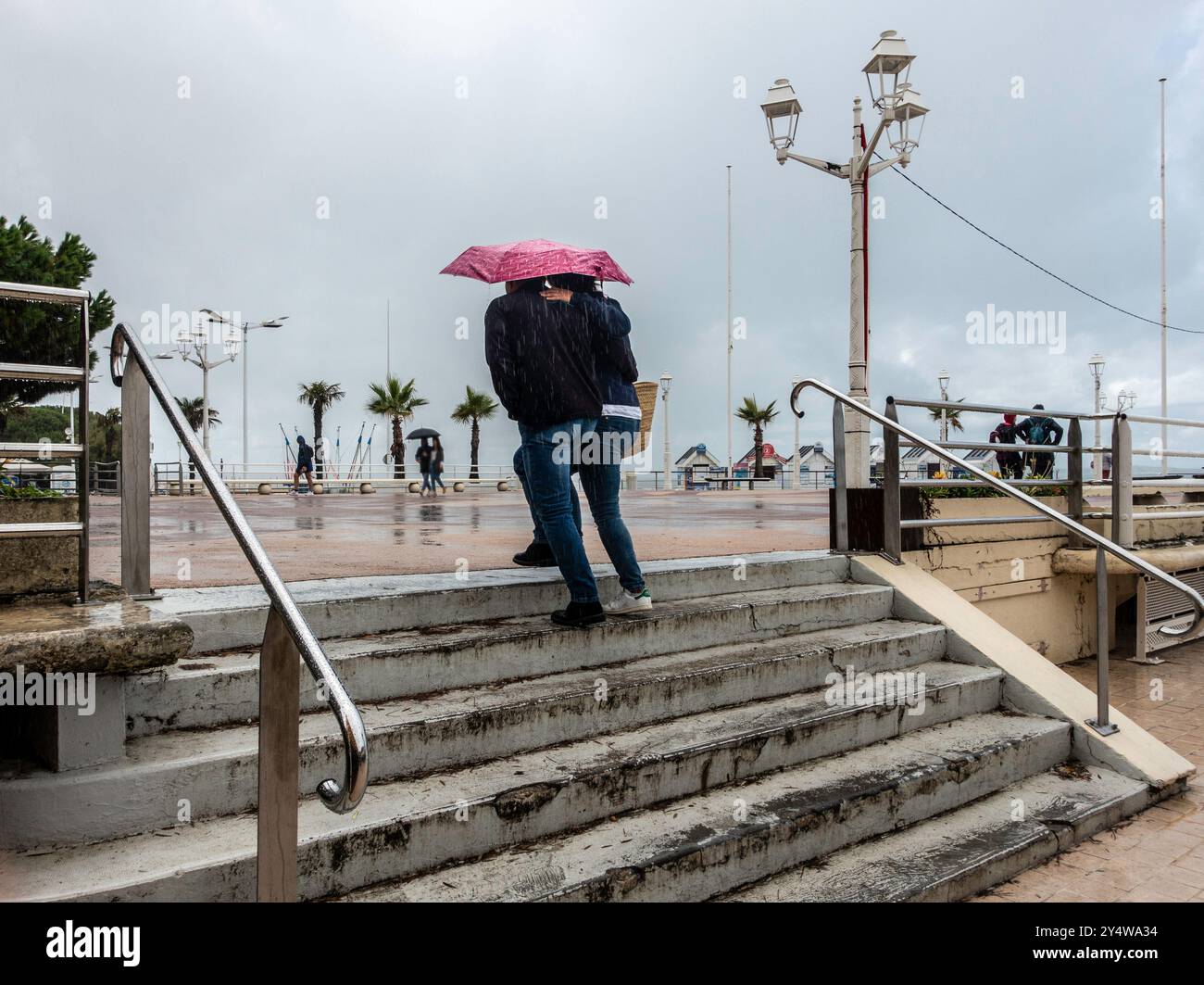 Ein Paar macht sich an einem trostlosen regnerischen Tag auf nasse Stufen und teilt sich einen rosafarbenen Regenschirm, wenn der Regen sanft fällt. Stockfoto