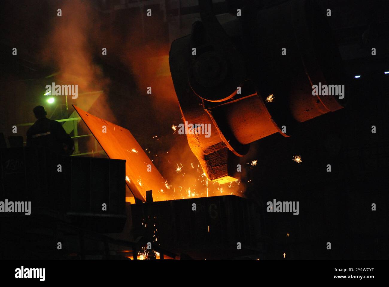 Das Bild zeigt eine dramatische Szene in einer Gießerei oder einem Stahlwerk, bei der geschmolzenes Metall aus einer großen Pfanne in eine Form oder gegossen wird Stockfoto